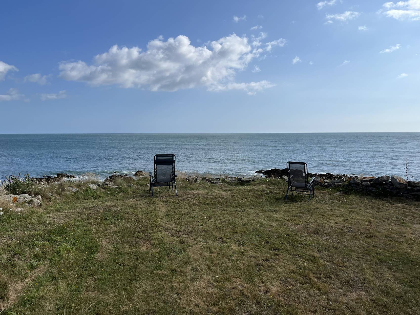 Zwei Liegestühle nebeneinander auf einer Wiese über dem Meer